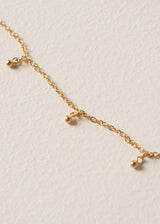 Close up detail of long golden chain necklace with gold beads and a black pendant