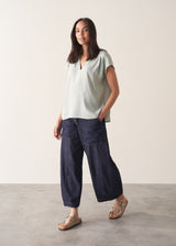 Woman wearing light green blouse and denim jeans against a plain background.