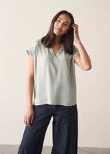 Woman wearing light green blouse and denim jeans against a plain background.