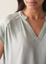 Woman wearing light green blouse and denim jeans against a plain background.
