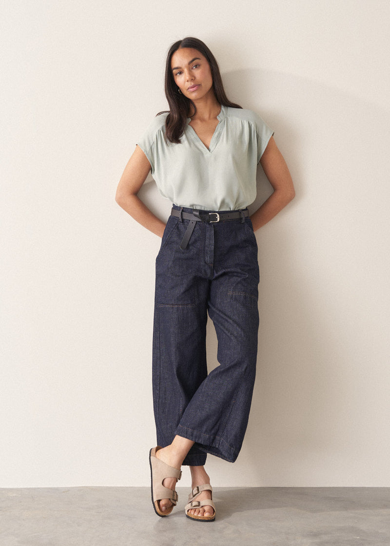 Woman wearing light green blouse and denim jeans against a plain background.