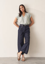 Woman wearing light green blouse and denim jeans against a plain background.