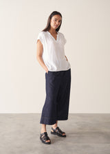 Woman wearing a white blouse and denim cullottes against a plain background