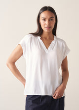 Woman wearing a white blouse and denim cullottes against a plain background