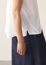 Woman wearing a white blouse and denim cullottes against a plain background