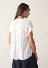 Woman wearing a white blouse and denim cullottes against a plain background