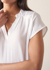 Woman wearing a white blouse and denim cullottes against a plain background