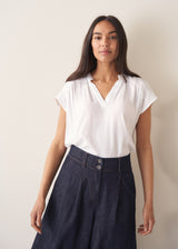 Woman wearing a white blouse and denim cullottes against a plain background