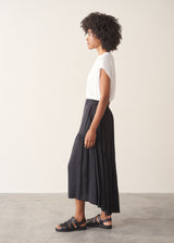 Woman wearing a white top and black satin tiered midi skirt against a plain background