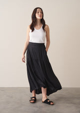 Woman wearing a black satin tiered midi skirt with a white tank top and black sandals