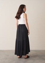Woman wearing a black satin tiered midi skirt with a white tank top and black sandals