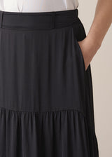 Woman wearing a black satin tiered midi skirt with a white tank top and black sandals