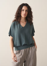 Woman wearing a teal v-neck sweater and checked barrel leg trousers 