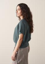 Woman wearing a teal v-neck sweater and checked barrel leg trousers 