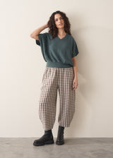 Woman wearing a teal v-neck sweater and checked barrel leg trousers with chunky black boots