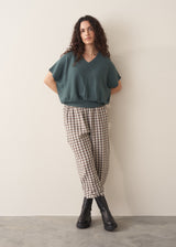 Woman wearing a teal v-neck sweater and checked barrel leg trousers with black boots