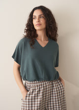 Woman wearing a teal v-neck sweater and checked barrel leg trousers 