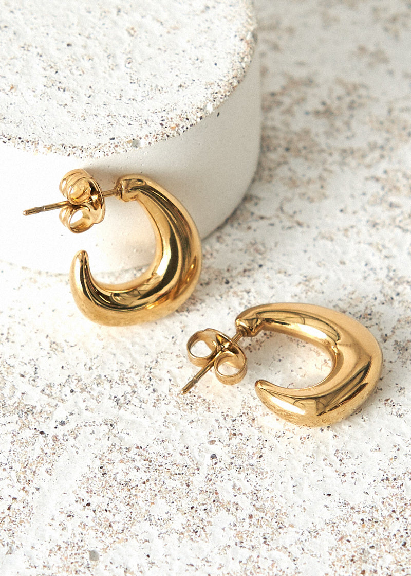 Chunky gold structured hoop earrings on cement background