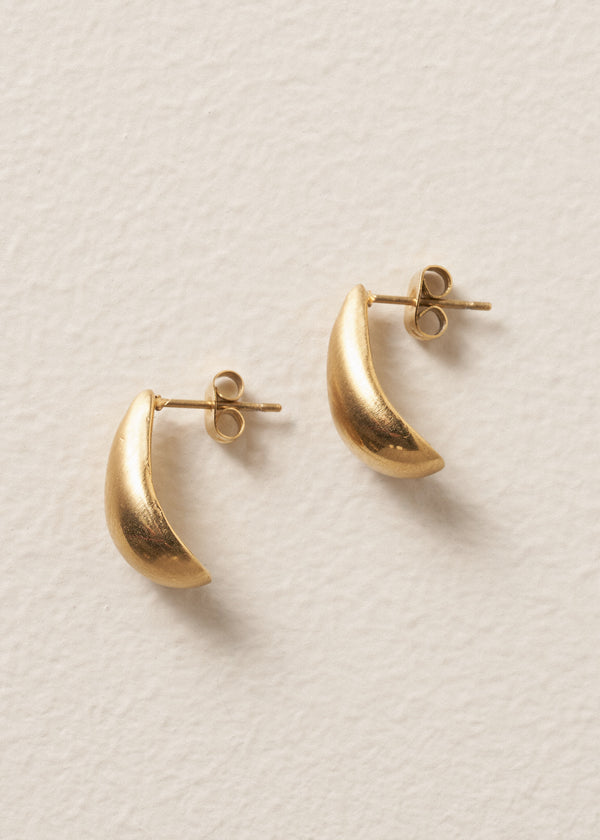 Side view of pair of brushed gold stud earrings in the shape of a teardrop, on beige background