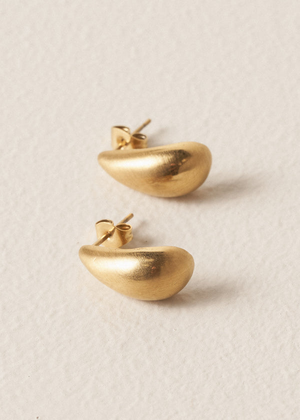 Pair of brushed gold stud earrings in the shape of a teardrop, on beige background