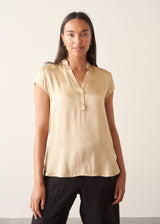 A woman wearing a short-sleeve yellow gold blouse and black trousers.