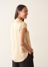 A woman wearing a short-sleeve yellow gold blouse and black trousers.