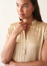 A woman wearing a short-sleeve yellow gold blouse and black trousers.