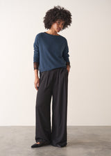 Person wearing a blue cashmere blend sweater and black wide leg trousers on a plain background