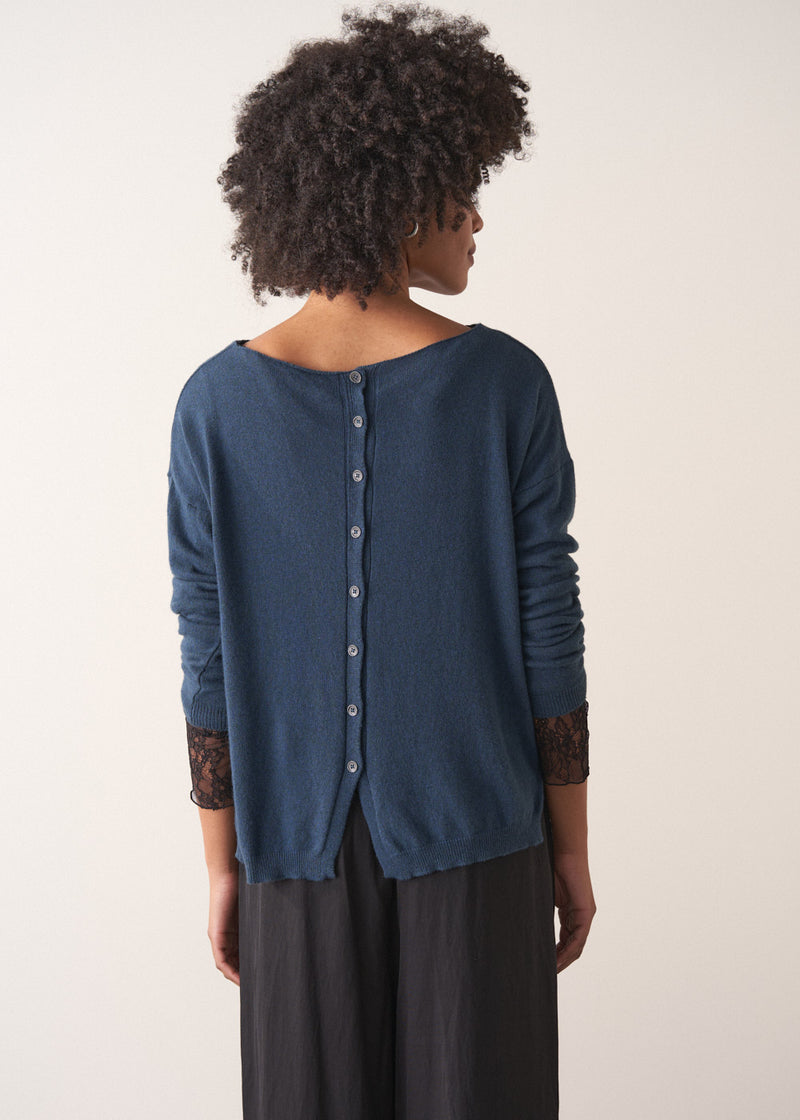 Person wearing a blue cashmere blend sweater and black wide leg trousers on a plain background