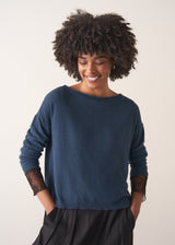 Person wearing a blue cashmere blend sweater and black wide leg trousers on a plain background