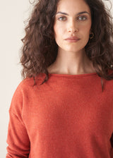 Woman wearing a red cashmere sweater and beige linen trousers against a plain background