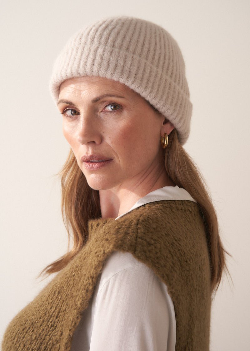 Woman wearing an oatmeal alpaca blend beanie hat with khaki jumper and white blouse