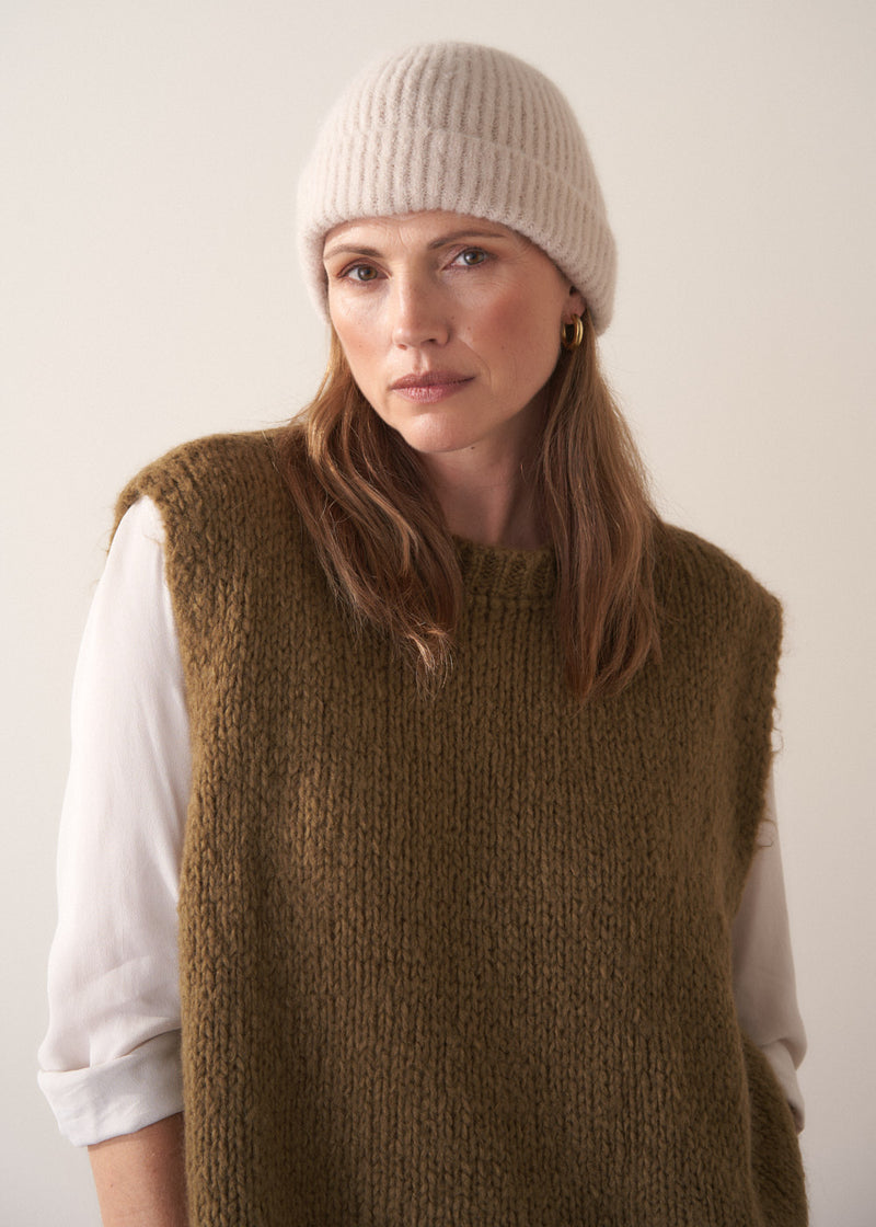Woman wearing a cream, super soft, alpaca wool blend beanie hat, styled with khaki sweater and white top