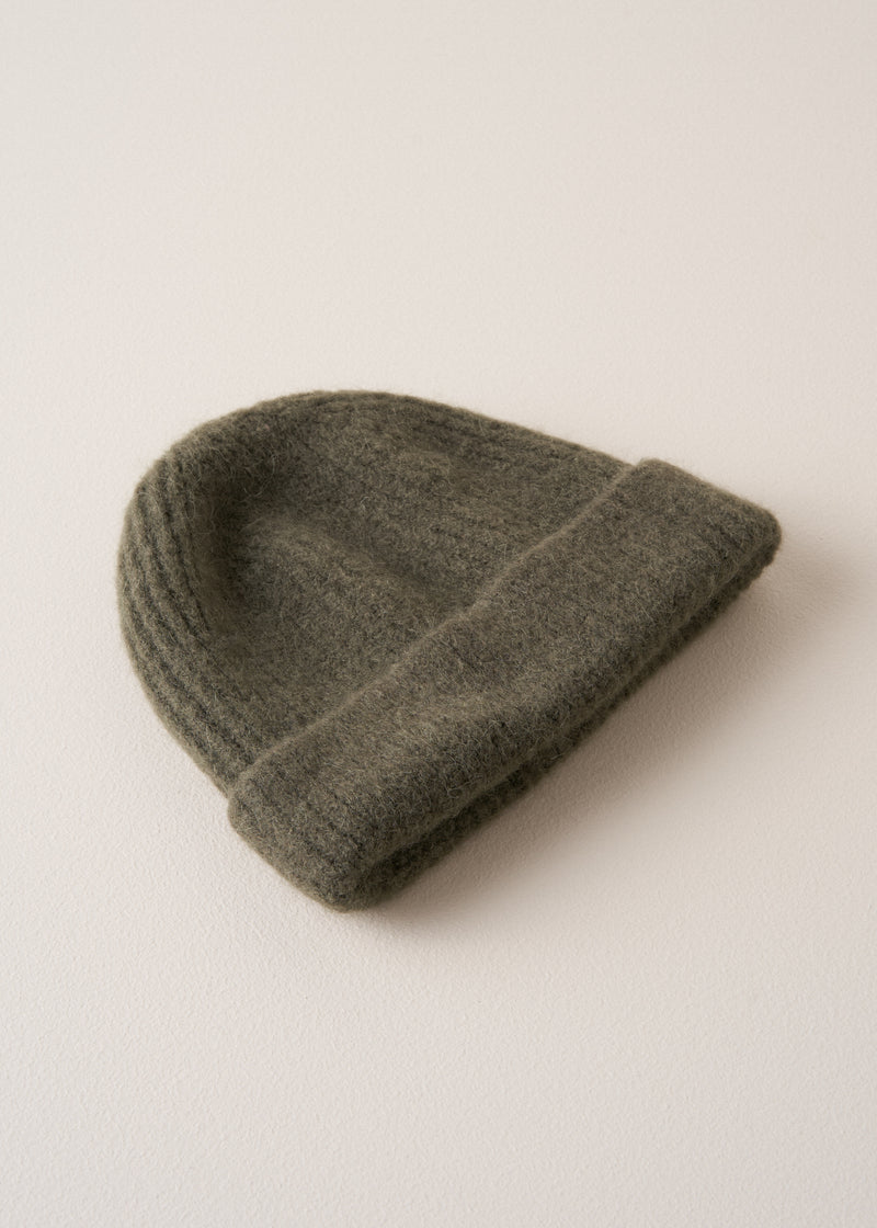 A super soft, alpaca wool blend beanie in khaki, styled on a beige background