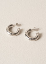 Pair of silver twist hoop earrings laid on a beige background