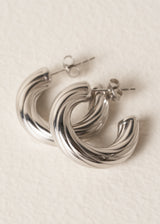 Stacked pair of silver twist hoop earrings on a beige background