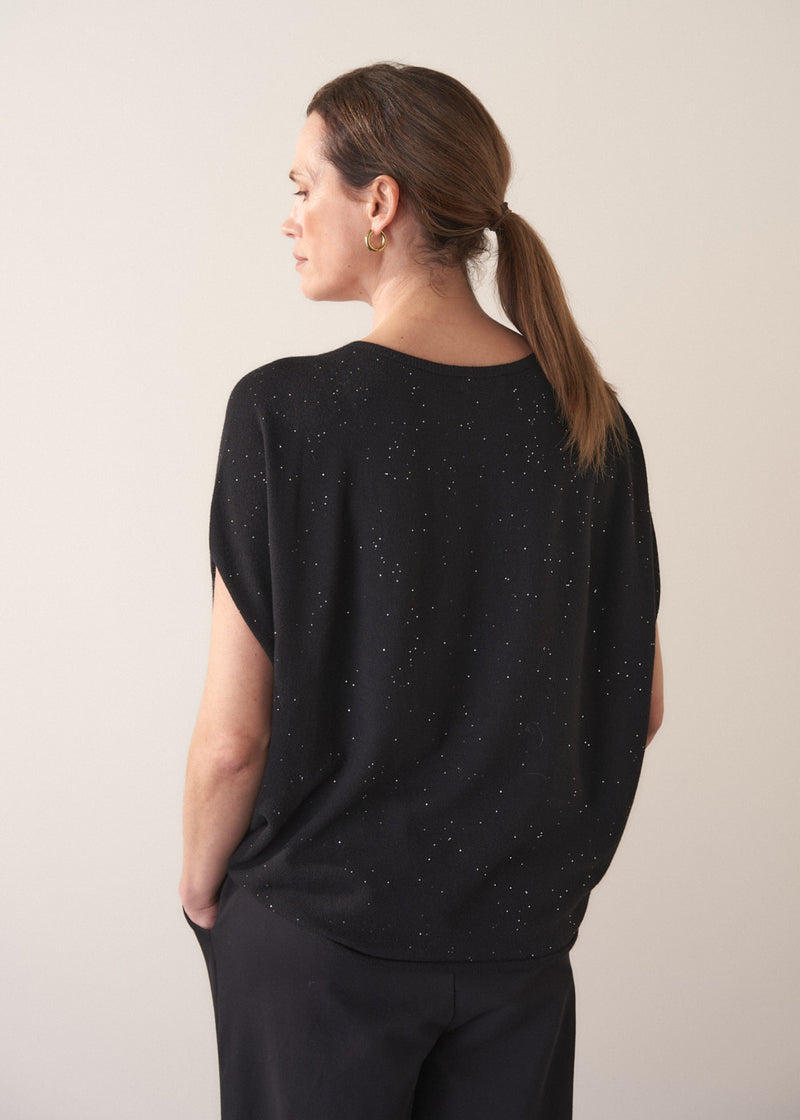 Woman wearing a black jumper with subtle sequin detail against a plain background