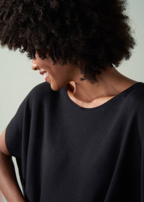 Close up of woman wearing a black sleeveless jumber against a neutral background
