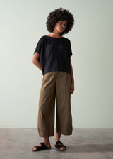 Woman wearing a black sleeveless sweater and brown trousers against a plain background