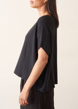 A woman wearing a black short-sleeve boat-neck sweater with black wide-leg trousers.