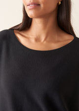 A woman wearing a black short-sleeve boat-neck sweater with black wide-leg trousers.