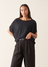 A woman wearing a black short-sleeve boat-neck sweater with black wide-leg trousers.