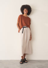 Woman wearing a light brown knitted top with a cream linen maxi skirt.