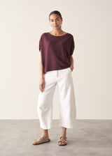 Woman wearing aubergine short sleeve knitted sweater and white barrel leg jeans