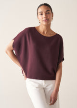 Woman wearing aubergine short sleeve knitted sweater and white barrel leg jeans