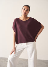 Woman wearing aubergine short sleeve knitted sweater and white barrel leg jeans