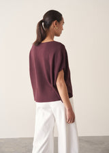 Woman wearing aubergine short sleeve knitted sweater and white barrel leg jeans
