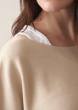 Woman wearing light oatmeal sleeveless sweater and dark green trousers