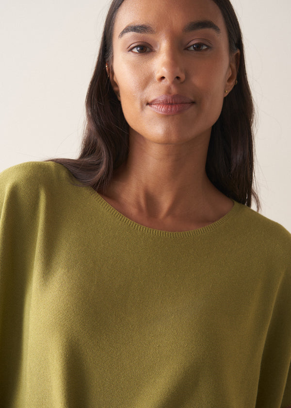 Woman wearing olive green short sleeve sweater against a plain background