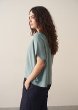 Woman wearing sage short sleeve draped sweater with blue jeans